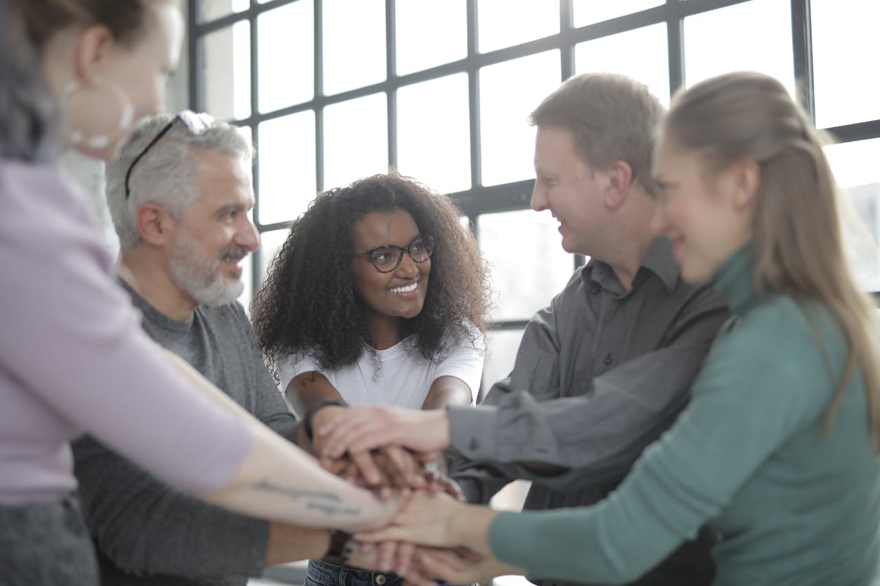 portfolio-01 Confident and smiling multiethnic colleagues joining hands and looking at each other while standing near big fenced window in afternoon
