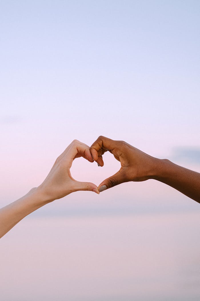 gallery-04 A powerful image of unity and diversity with two hands forming a heart against a serene pastel sky.