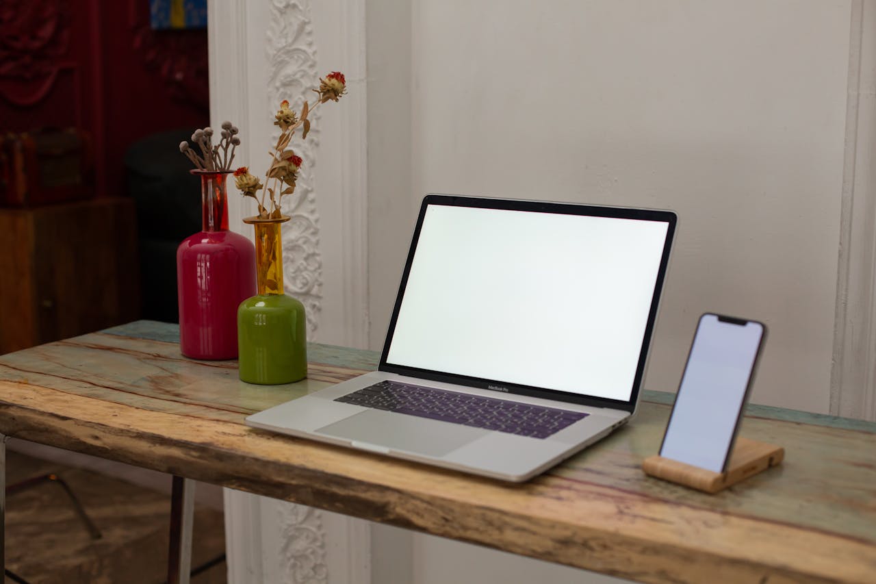 gallery-06 Laptop and smartphone on a rustic desk with decorative vases in a cozy indoor setting.